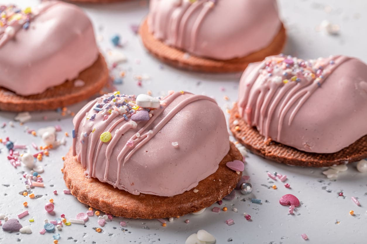 Heart-shaped pink cookies with drizzle and sprinkles on a wooden surface.