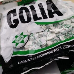 A bag of Golia candies, partially opened, revealing individually wrapped candies inside. The packaging design includes green, black, and white colors, and the text on the bag is in Italian, highlighting the flavor as licorice.